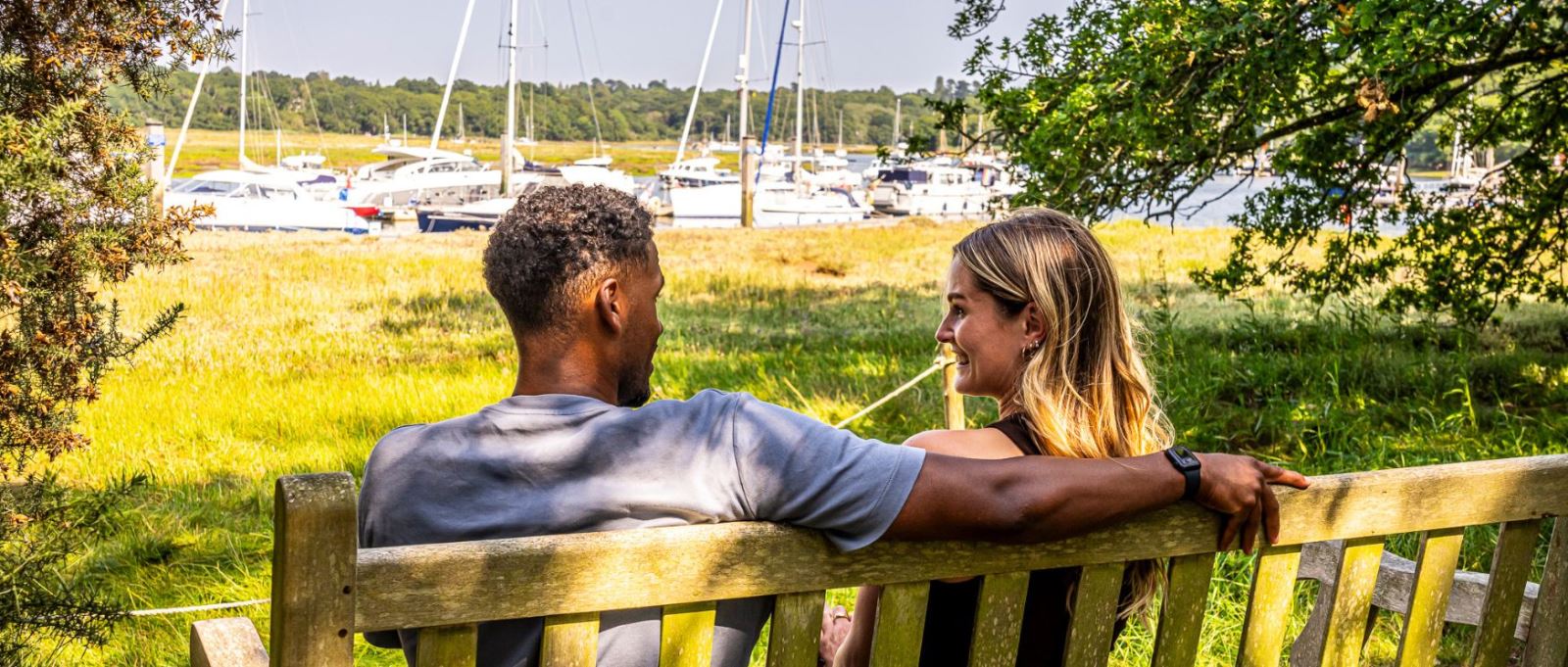 A couple sit on a bench overlooking the Beaulieu River at Buckler's Hard